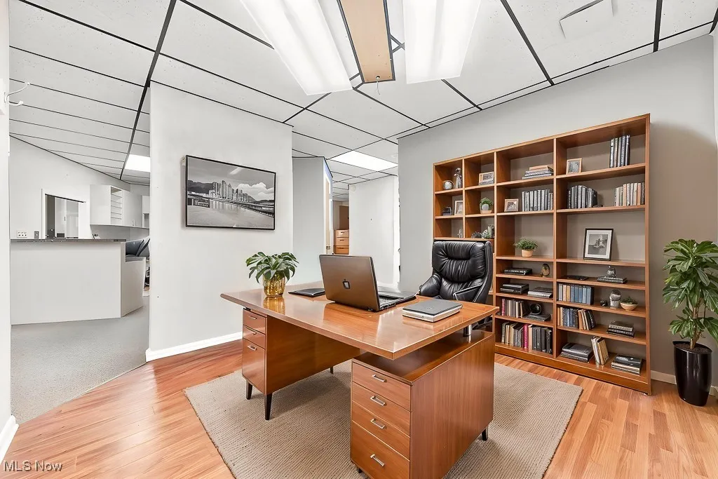 Office area with light wood-style floors, baseboards, and a paneled ceiling