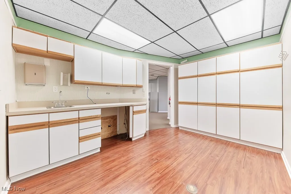 Kitchen featuring a sink, white cabinetry, light countertops, and light wood-type flooring