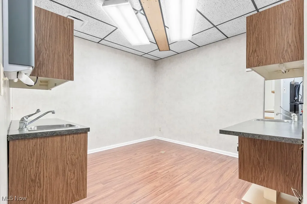Kitchen featuring a paneled ceiling, dark countertops, light wood finished floors, and a sink