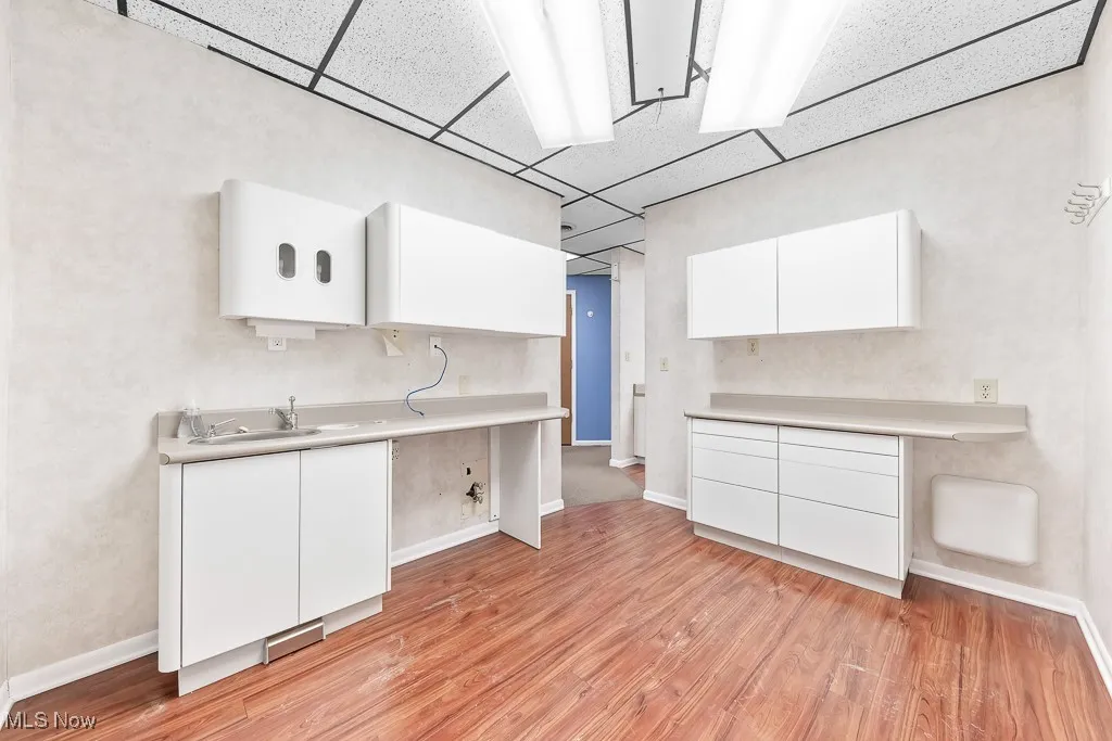 Kitchen with a paneled ceiling, white cabinetry, a sink, and light countertops