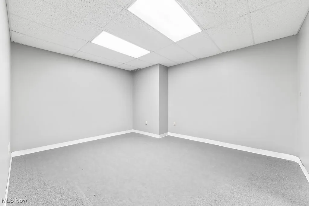 Carpeted spare room featuring a paneled ceiling and baseboards