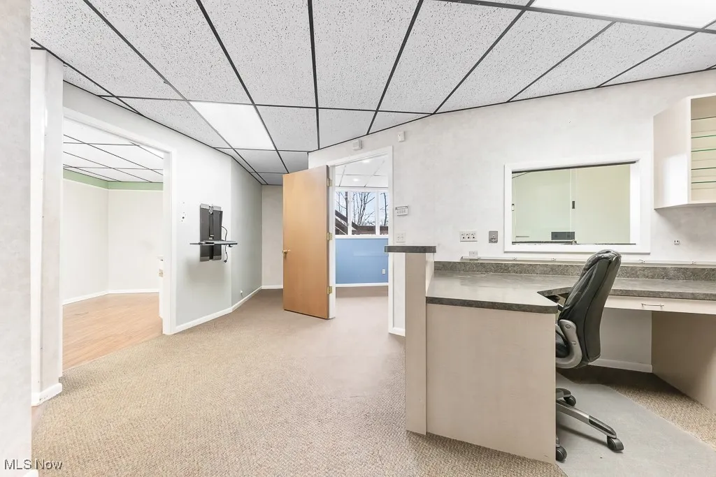 Unfurnished office featuring a paneled ceiling, built in desk, carpet, and baseboards