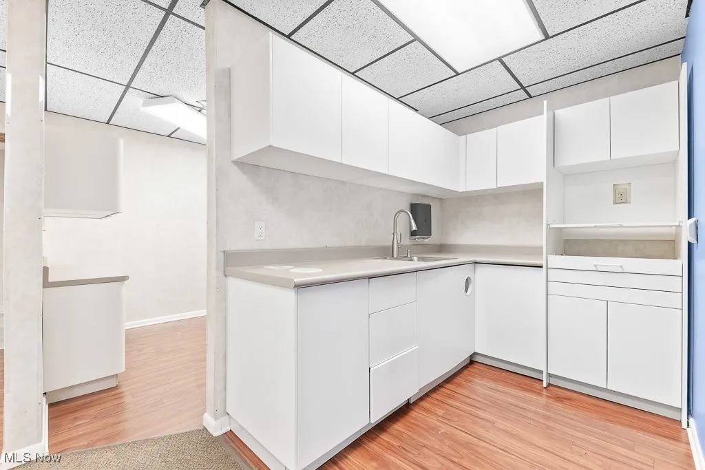 Kitchen featuring a sink, white cabinetry, light countertops, and a drop ceiling