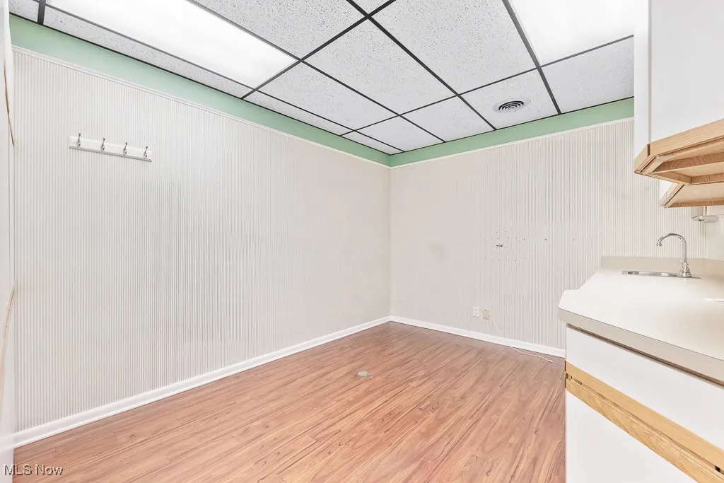 Empty room featuring a sink, visible vents, light wood-style flooring, a drop ceiling, and baseboards