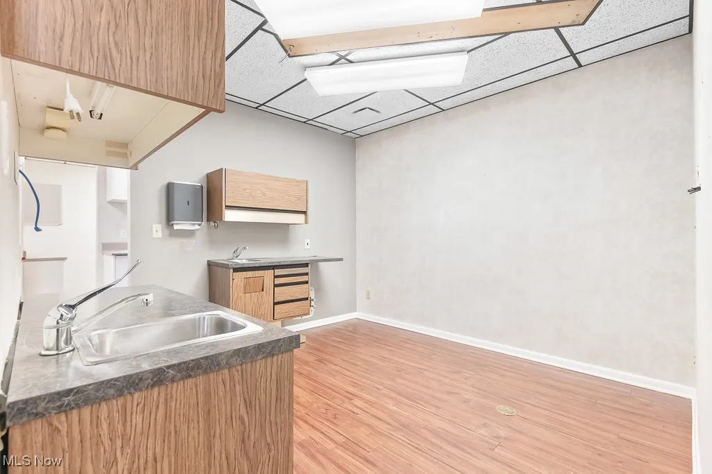 Kitchen featuring a sink, a paneled ceiling, baseboards, dark countertops, and light wood-style floors