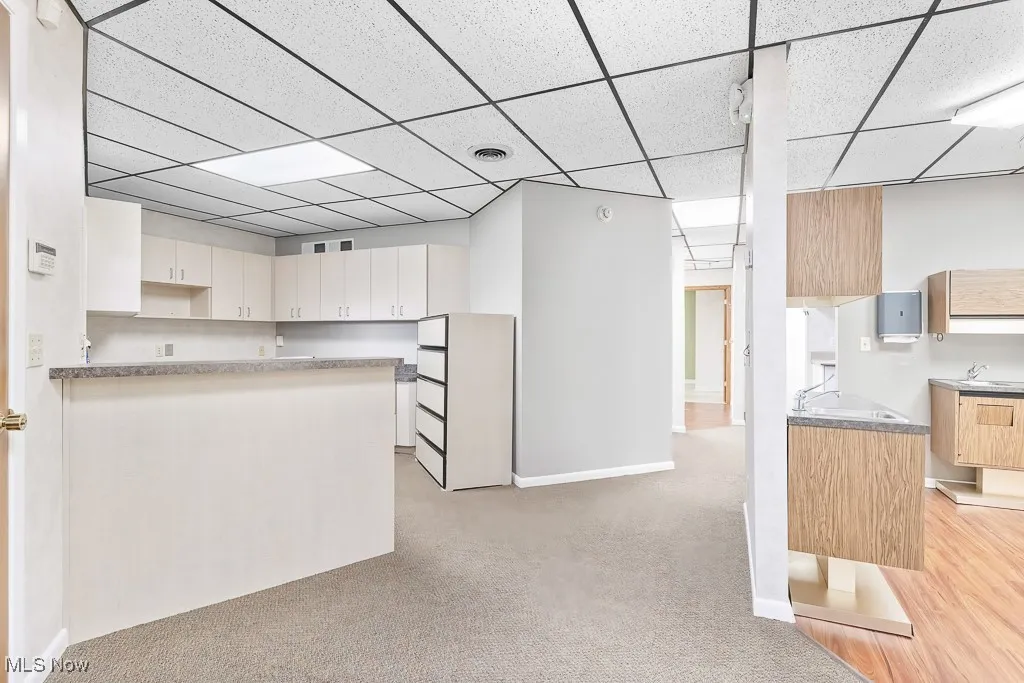 Kitchen featuring a paneled ceiling, white cabinets, visible vents, and light colored carpet