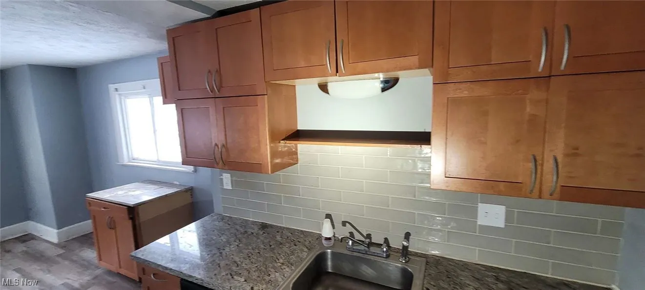 Kitchen featuring decorative backsplash, light stone counters, light wood-type flooring, and sink