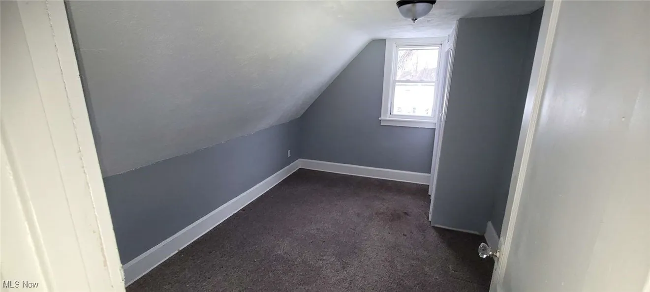 Bonus room with dark colored carpet, a textured ceiling, and lofted ceiling