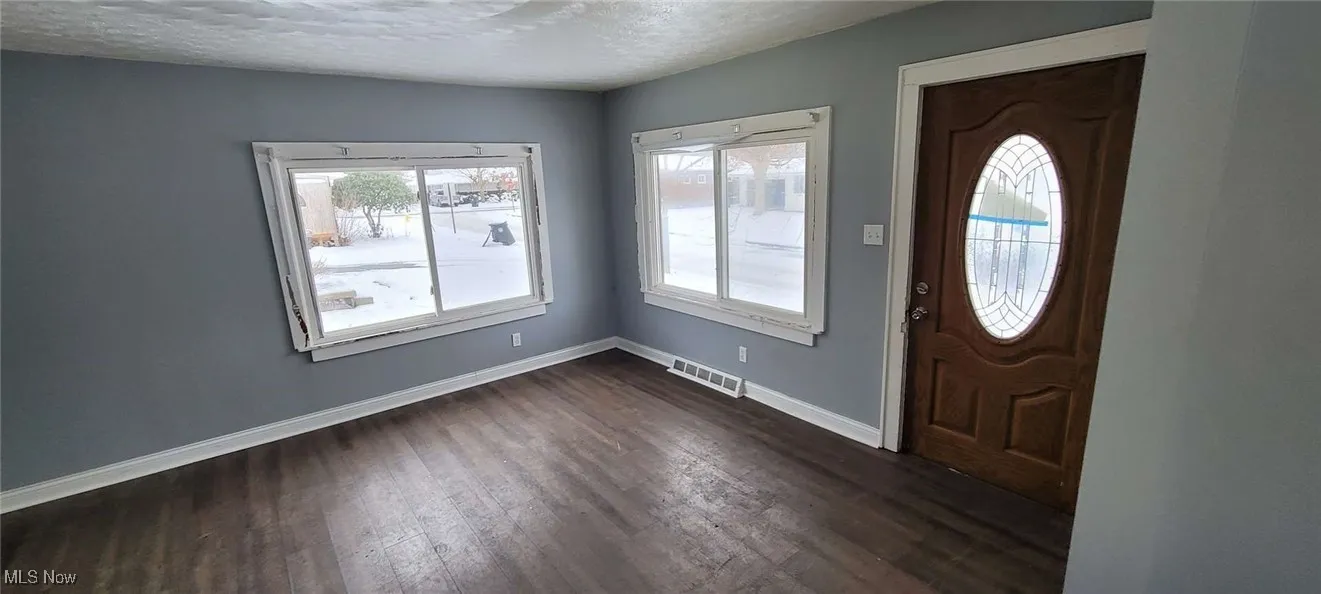 Entrance foyer with a textured ceiling, dark wood-type flooring, and a healthy amount of sunlight