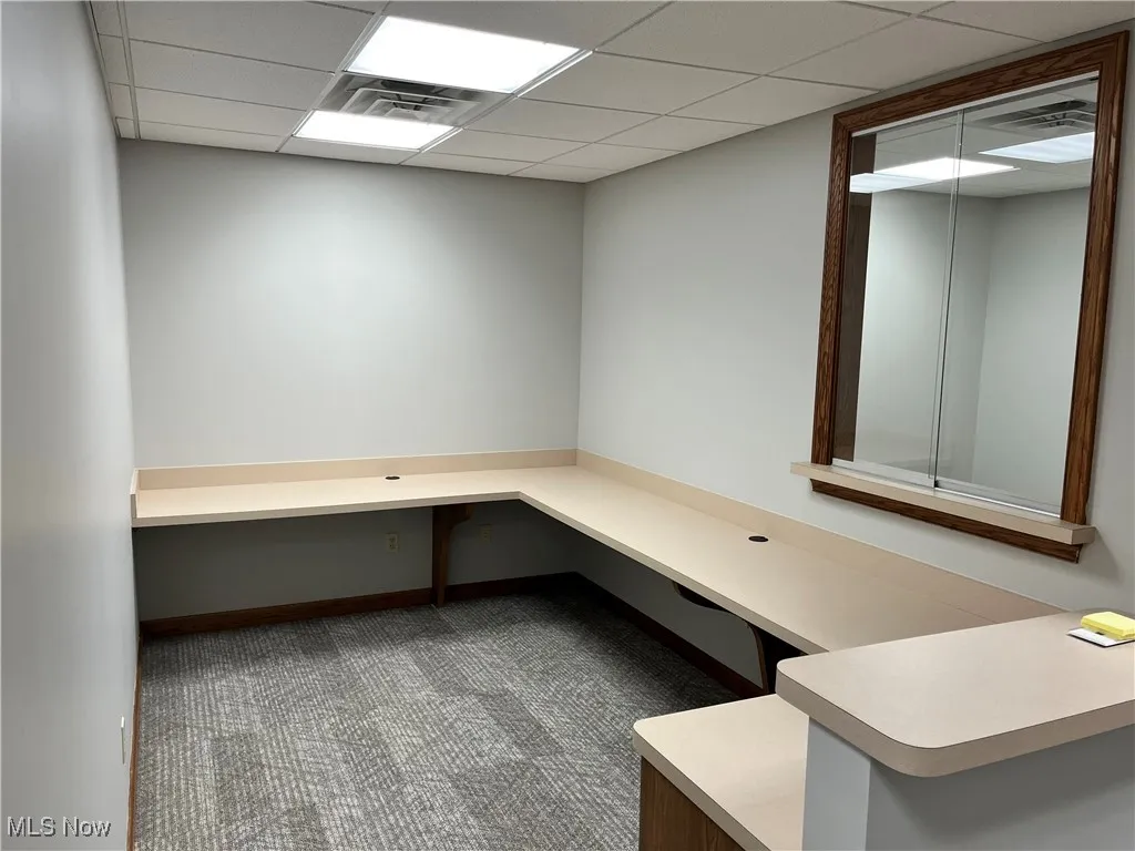 Unfurnished office featuring built in study area, carpet flooring, and a drop ceiling