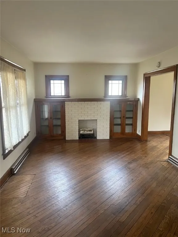 Unfurnished living room featuring dark wood-type flooring, a wealth of natural light, and a baseboard radiator