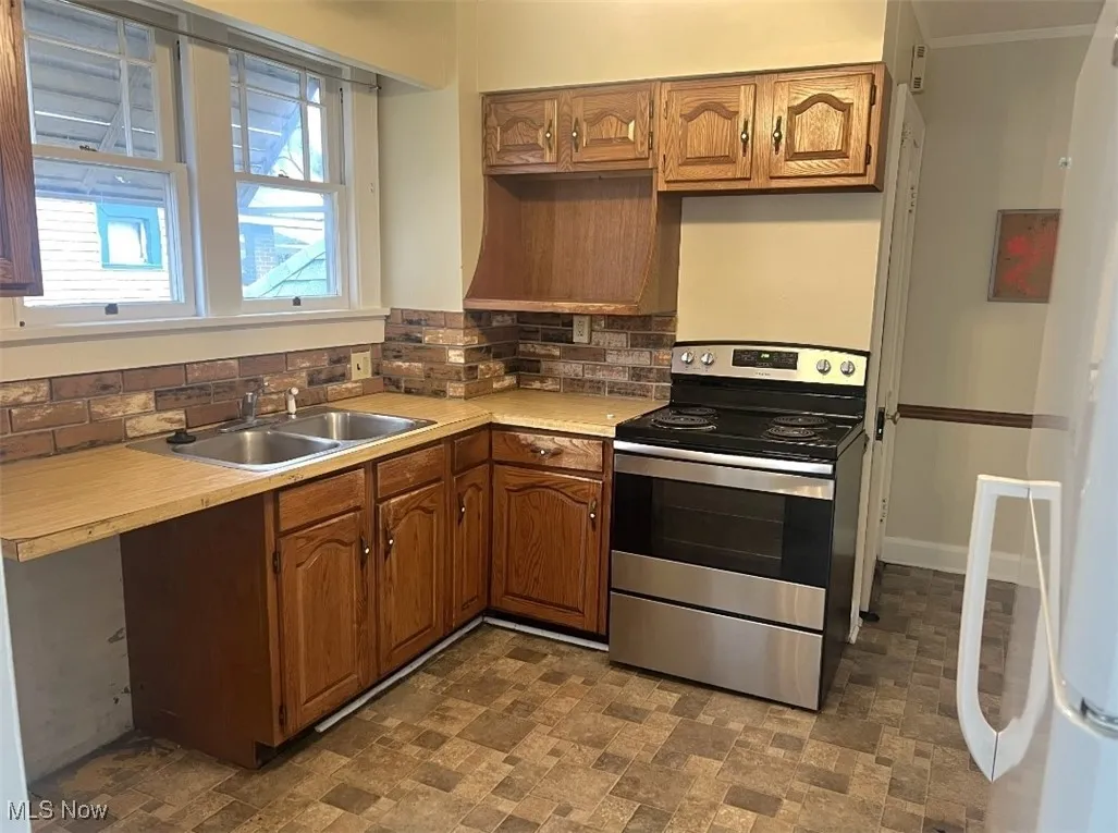 Kitchen featuring tasteful backsplash, ornamental molding, stainless steel electric stove, and sink