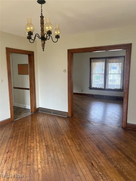 Spare room featuring baseboard heating, dark hardwood / wood-style flooring, and a chandelier