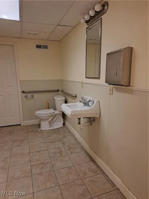 Bathroom featuring tile patterned floors, sink, a drop ceiling, and toilet