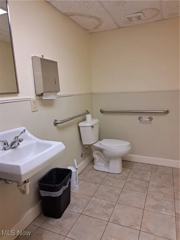 Bathroom with tile patterned flooring, toilet, a drop ceiling, and sink