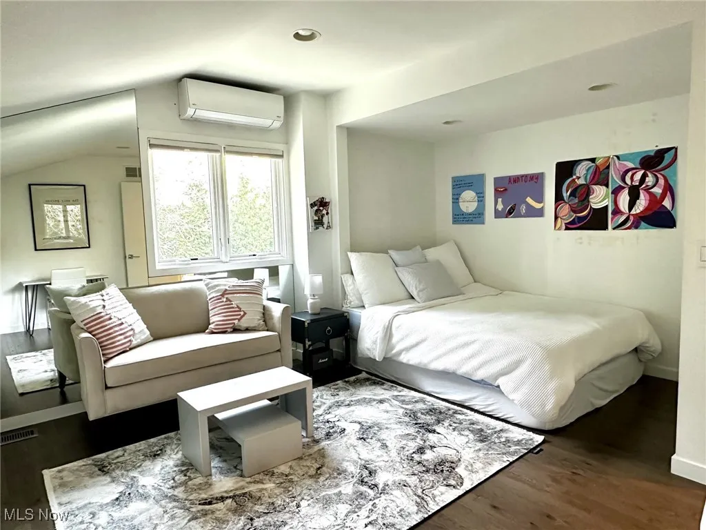 Bedroom with dark wood-type flooring, vaulted ceiling, and an AC wall unit