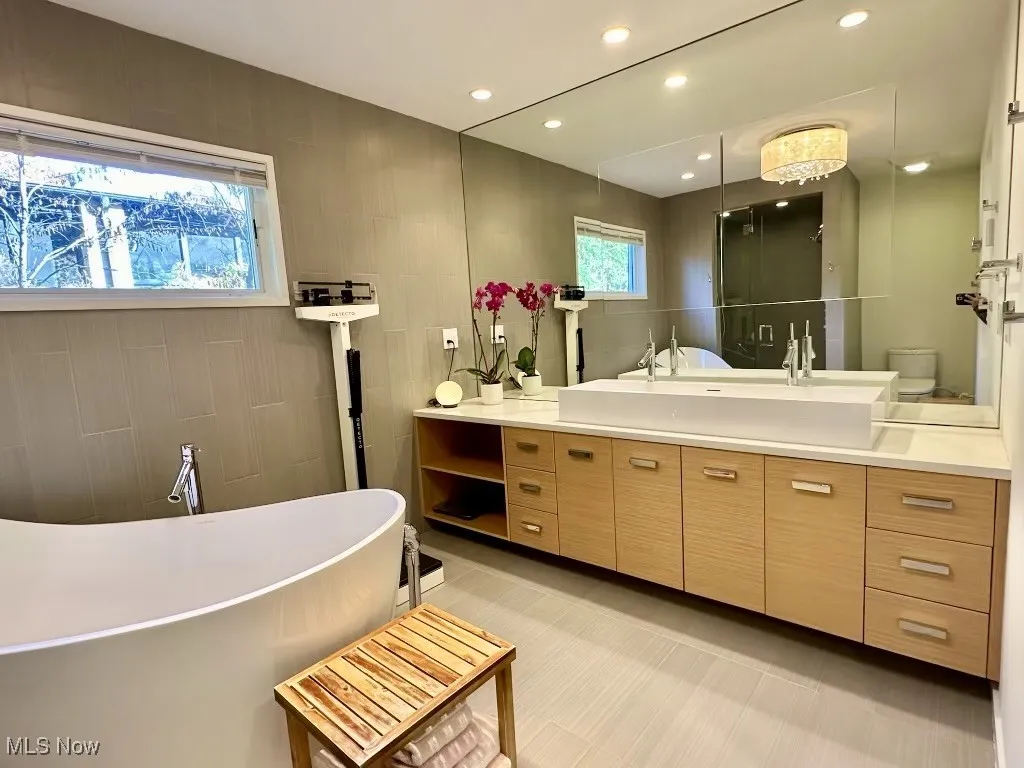 Bathroom featuring tile patterned flooring, toilet, vanity, tile walls, and a bathing tub
