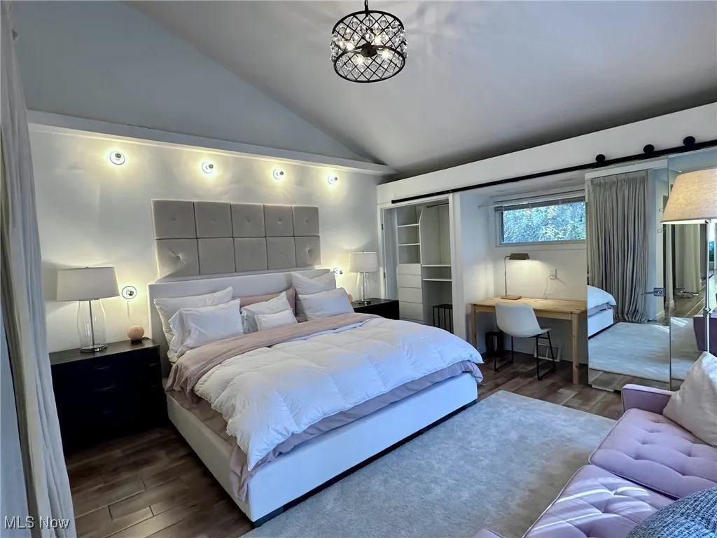Bedroom featuring an inviting chandelier, vaulted ceiling, a barn door, and dark hardwood / wood-style floors