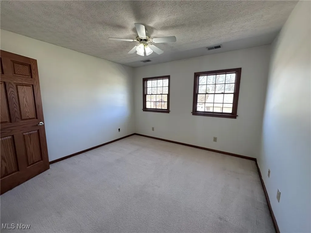 Empty room with visible vents, baseboards, light carpet, and ceiling fan