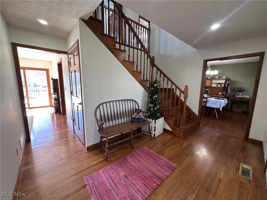 Corridor featuring stairway, wood finished floors, baseboards, visible vents, and a textured ceiling