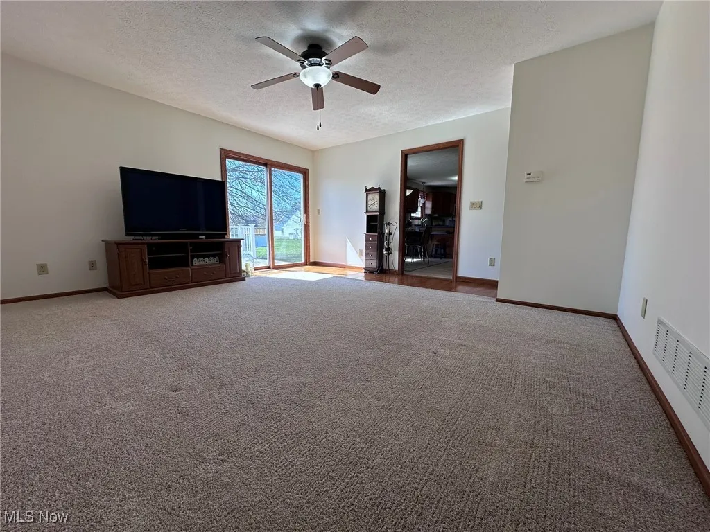 Unfurnished living room with visible vents, baseboards, carpet flooring, a textured ceiling, and a ceiling fan
