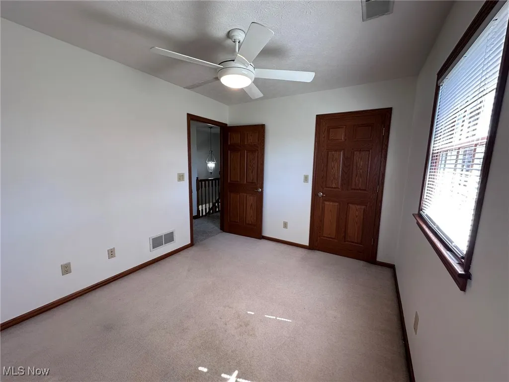 Unfurnished bedroom with visible vents, light colored carpet, baseboards, and ceiling fan