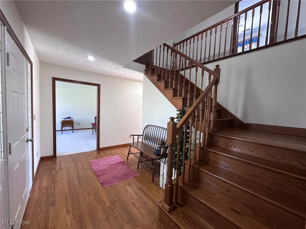 Stairway featuring recessed lighting, a textured ceiling, baseboards, and wood finished floors