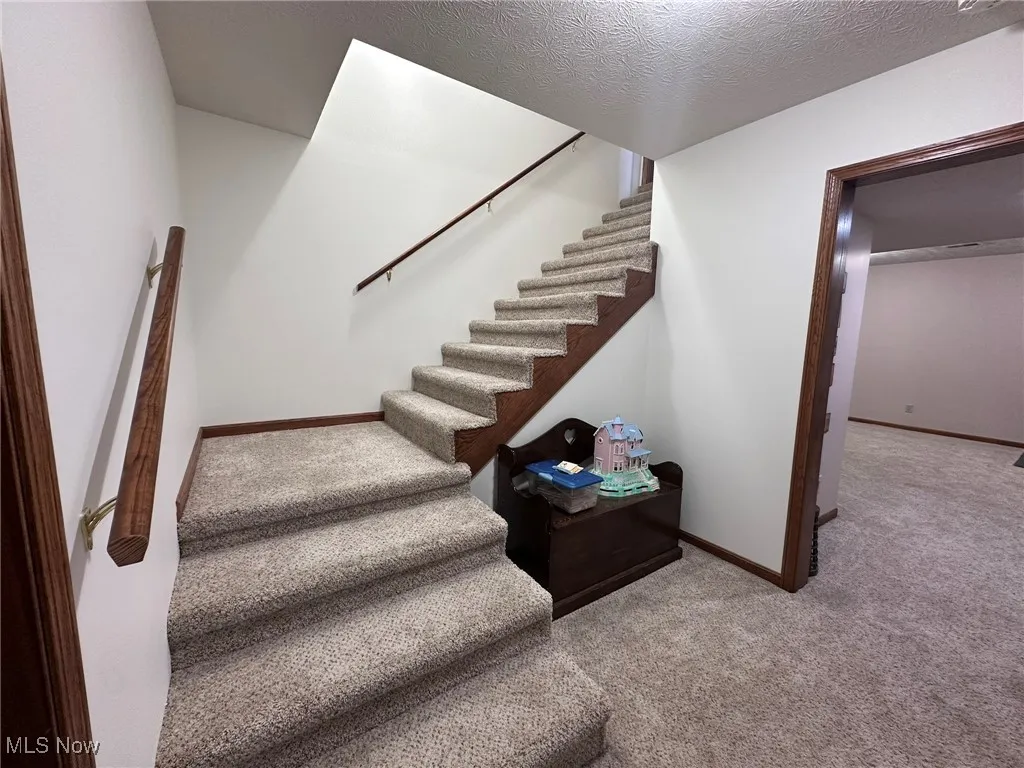 Staircase featuring baseboards, carpet, and a textured ceiling