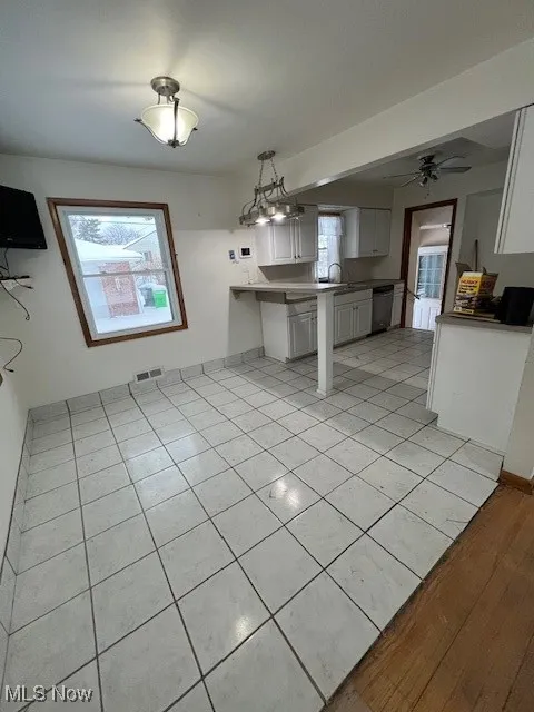 Kitchen featuring kitchen peninsula, hanging light fixtures, dishwashing machine, plenty of natural light, and white cabinets