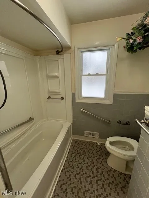 Bathroom featuring toilet, tile walls, and shower / tub combination