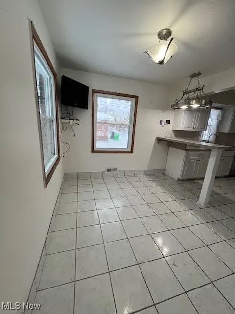 Kitchen featuring white cabinets, pendant lighting, kitchen peninsula, and light tile patterned floors