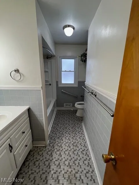 Full bathroom with tile walls, shower / bath combination, toilet, and vanity