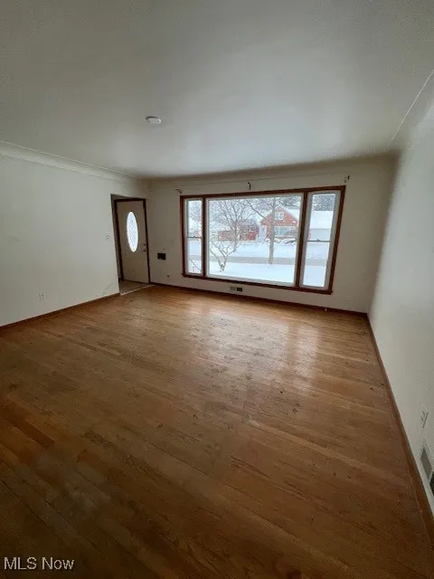 Unfurnished living room featuring hardwood / wood-style flooring and crown molding