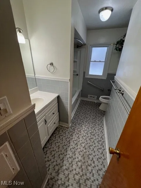 Full bathroom with toilet, vanity, tile walls, and  shower combination