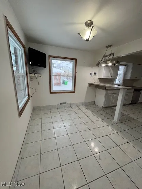 Kitchen featuring kitchen peninsula, light tile patterned floors, pendant lighting, white cabinets, and sink