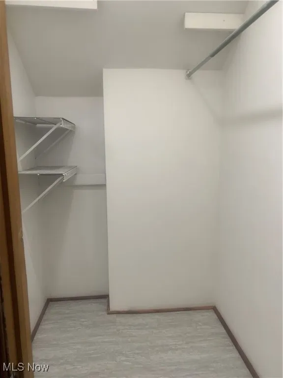 Walk in closet with light hardwood / wood-style flooring