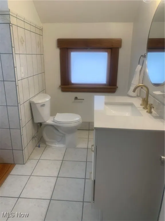 Bathroom with toilet, vaulted ceiling, tile patterned flooring, tile walls, and vanity