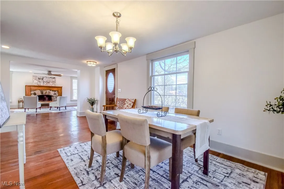 Dining space featuring ceiling fan with notable chandelier, a fireplace, light wood-type flooring, and baseboards