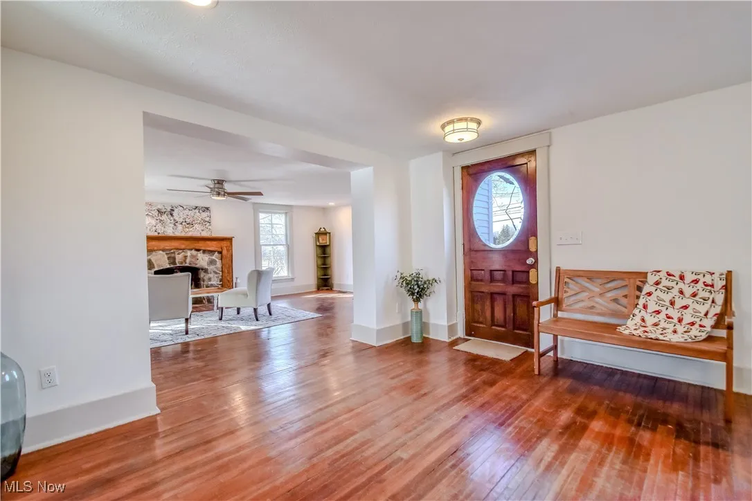 Foyer with a stone fireplace, ceiling fan, baseboards, and wood finished floors