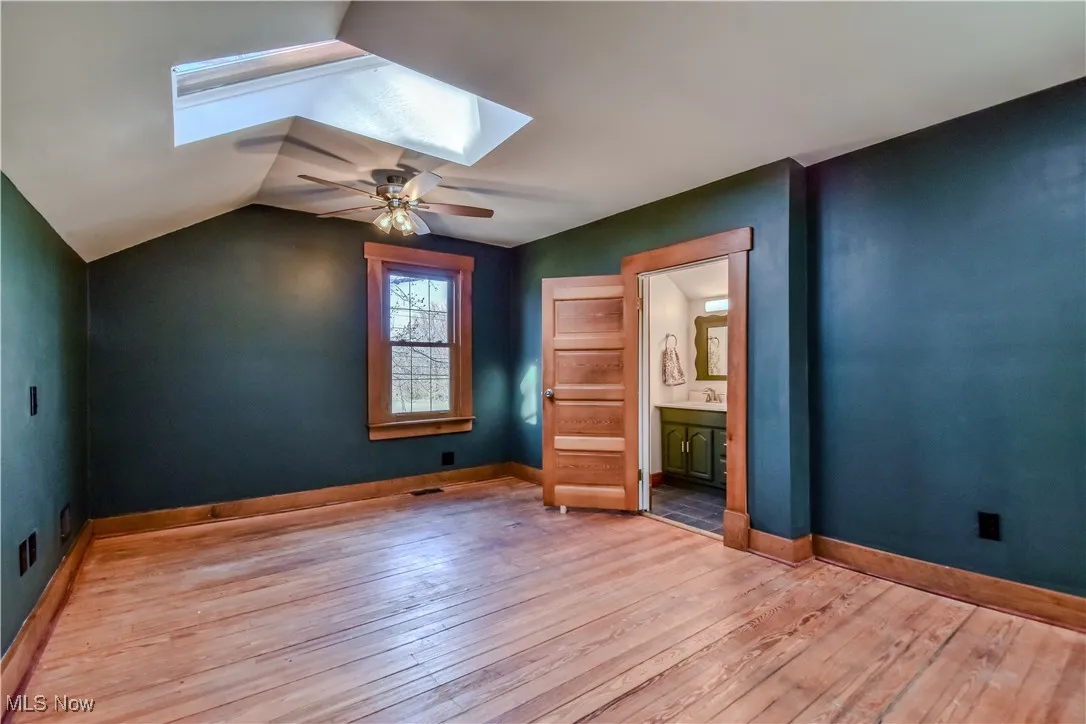Unfurnished bedroom with baseboards, a sink, ensuite bathroom, lofted ceiling with skylight, and light wood-type flooring
