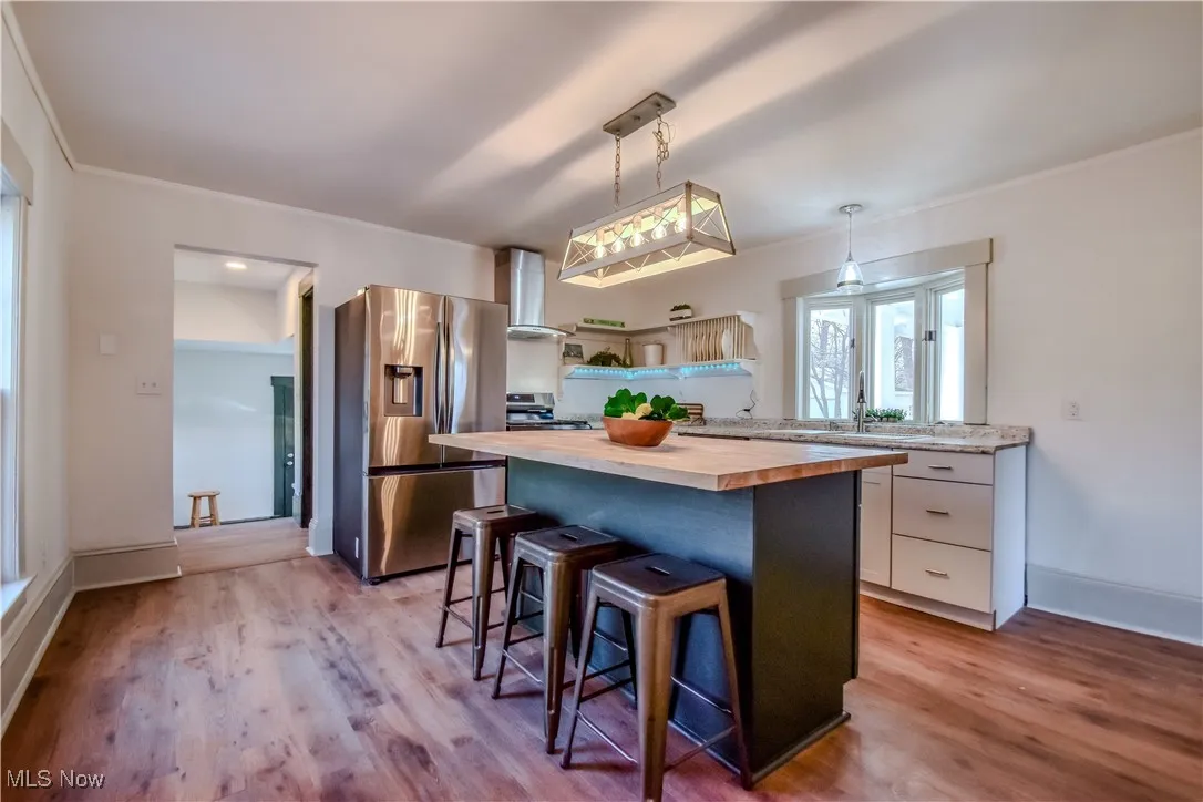 Kitchen with light wood-type flooring, a kitchen bar, white cabinetry, appliances with stainless steel finishes, and wooden counters