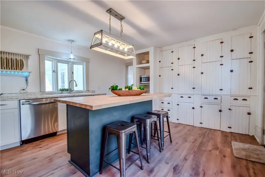 Kitchen featuring stainless steel dishwasher, light wood-type flooring, a kitchen bar, and wood counters