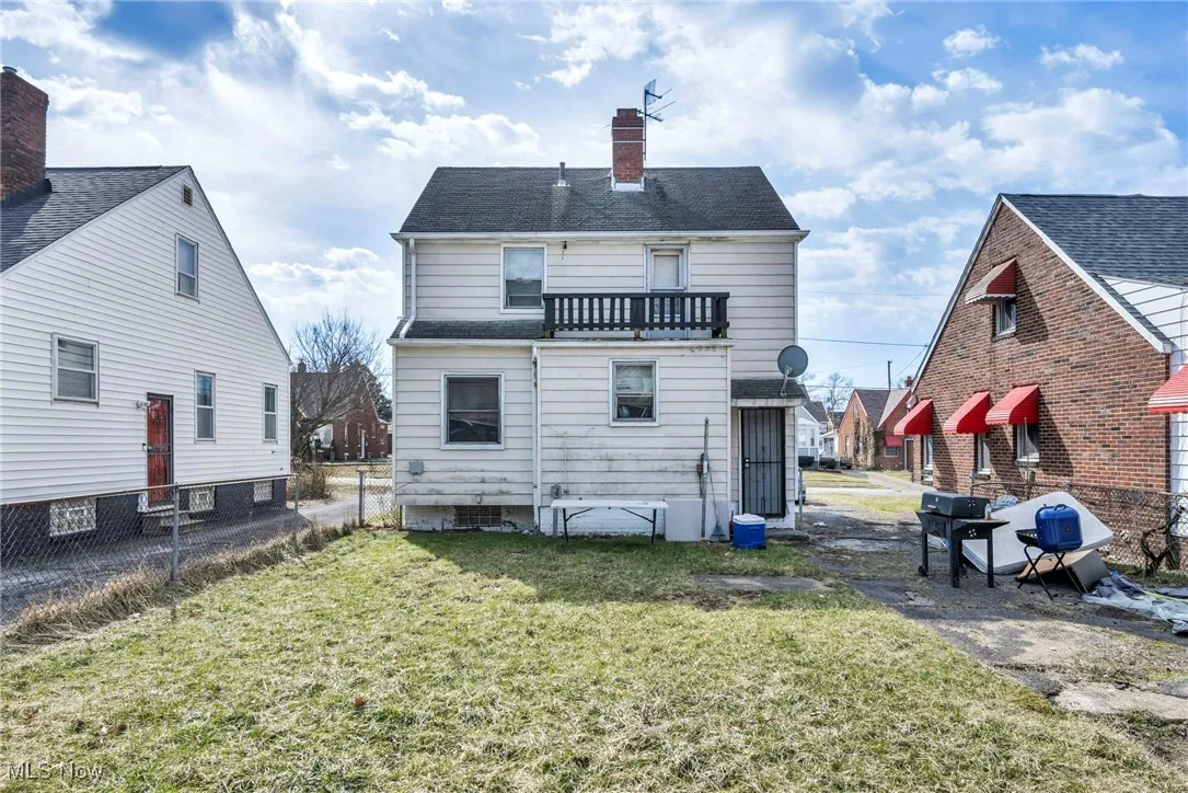 Back of house with fence, roof with shingles, a chimney, a balcony, and a yard