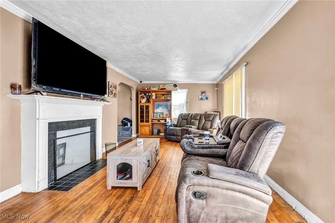 Living area featuring arched walkways, a fireplace, crown molding, and light wood-style floors