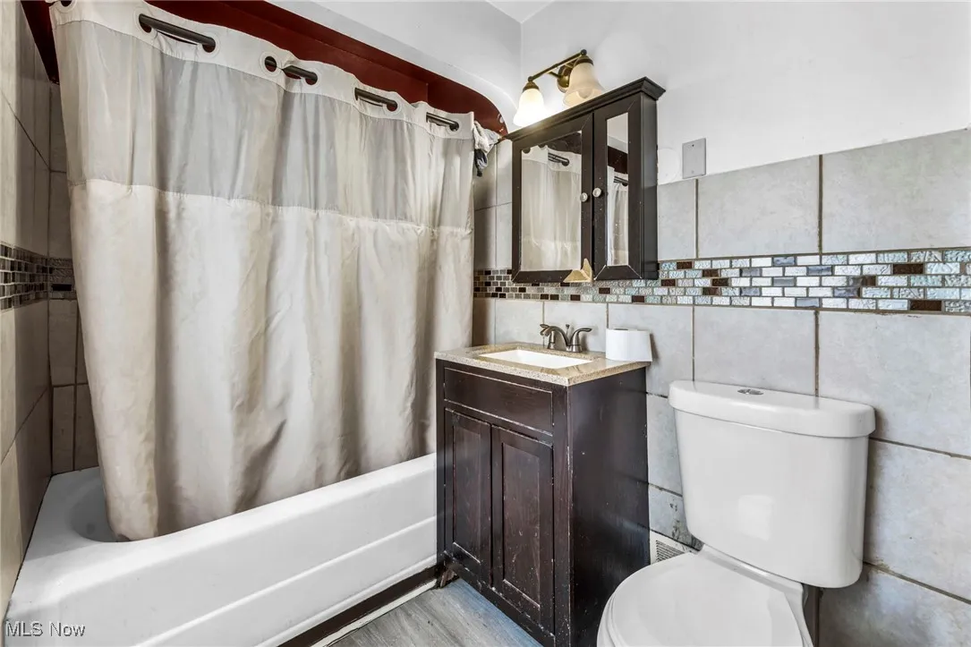 Bathroom with shower / bath combo with shower curtain, toilet, wood finished floors, tile walls, and vanity