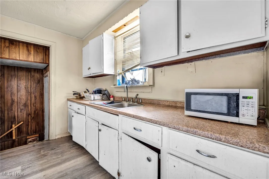Kitchen featuring white microwave, light wood-style flooring, white cabinetry, and a sink