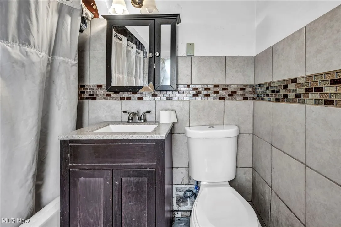 Full bath featuring a shower with curtain, toilet, tile walls, and vanity