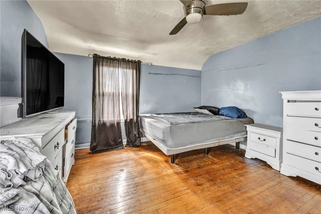 Bedroom with light wood finished floors, a textured ceiling, a ceiling fan, and vaulted ceiling