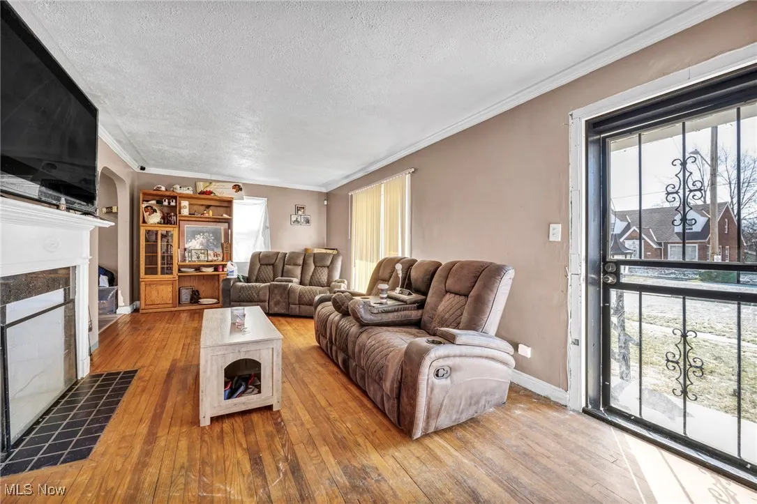 Living area featuring hardwood / wood-style floors, a fireplace, arched walkways, and ornamental molding