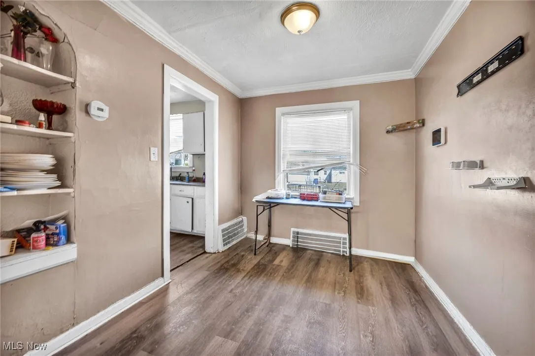 Hallway with visible vents, wood finished floors, baseboards, and ornamental molding